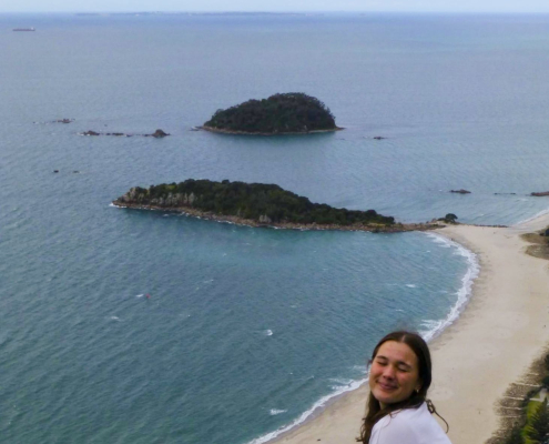 Mia sitzt auf der Kuppe des Mount Maunganui und blickt herab aufs Meer