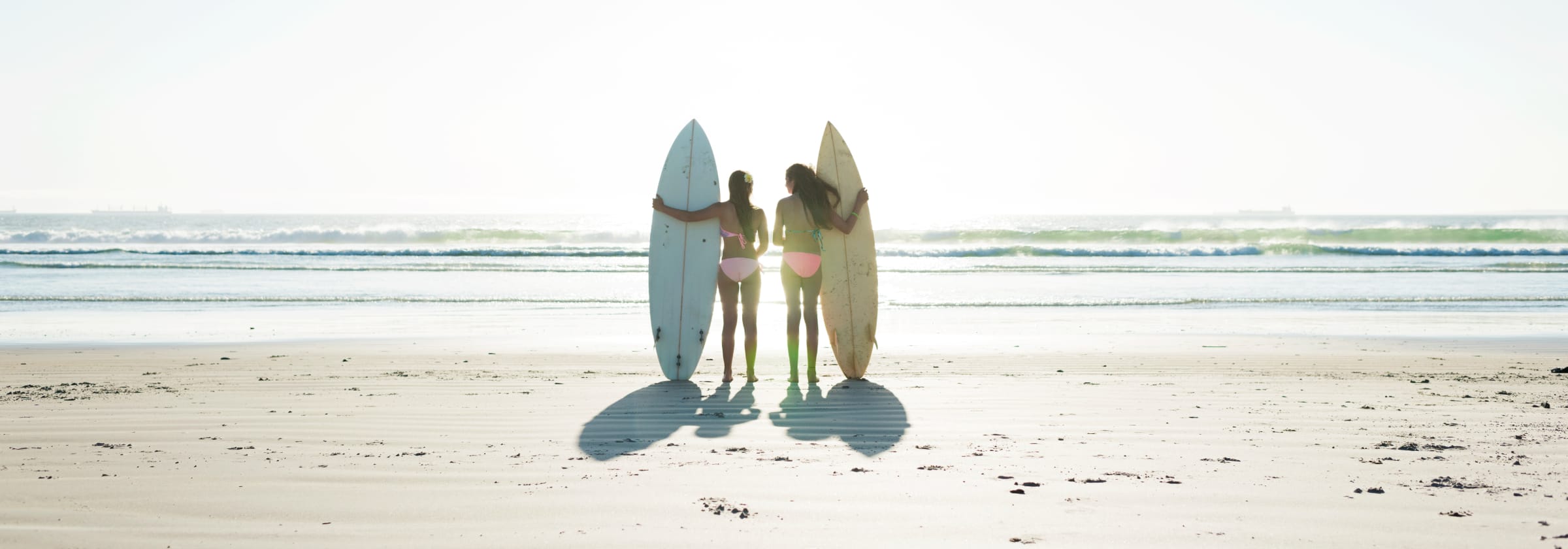 Zwei Mädchen stehen mit Surfboard am Strand